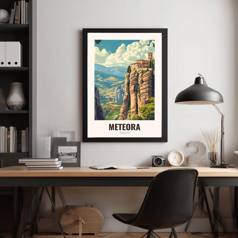 May include: A framed art print of Meteora, Greece. The image shows a monastery perched on a rock formation, with a valley and mountains in the background. The print is in a black frame, with the word "METEORA" printed at the bottom.