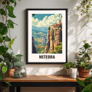 May include: A framed art print of Meteora, Greece. The image shows a monastery perched on a rock formation, with a colourful sky and valley. The print is in a black frame and includes the text "METEORA GREECE".