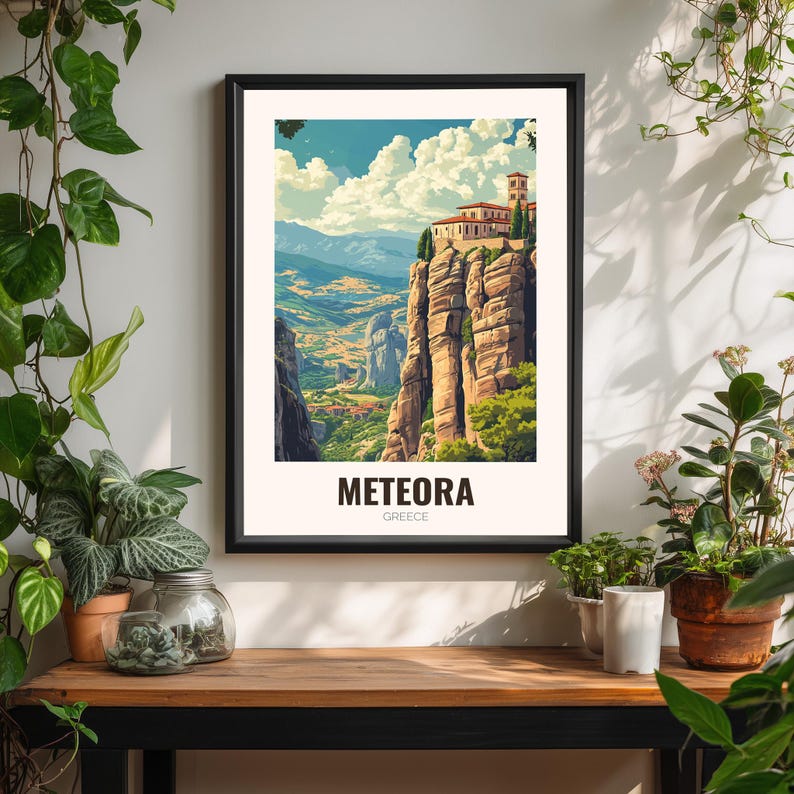 May include: A framed art print of Meteora, Greece. The image shows a monastery perched on a rock formation, with a colourful sky and valley. The print is in a black frame and includes the text "METEORA GREECE".