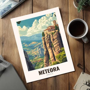 May include: A print depicting Meteora, Greece, with a monastery perched on a cliff edge. The artwork is in a vintage travel poster style, using blues, greens, and browns. The print is on a wooden surface, next to a cup of coffee.