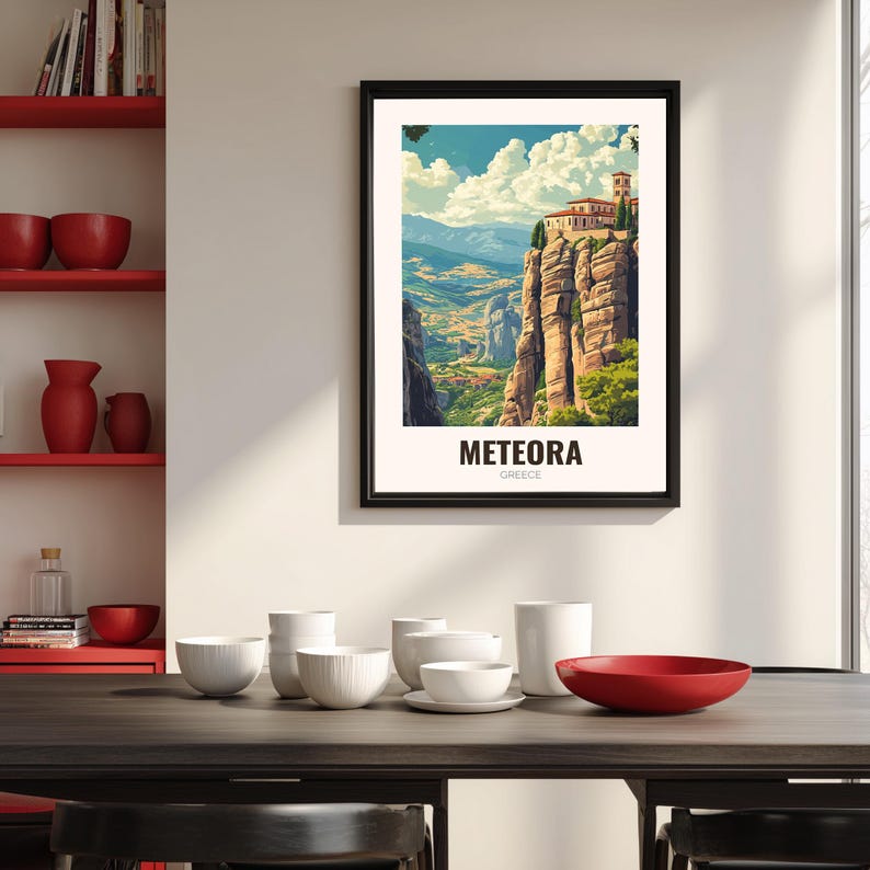 May include: A framed art print of Meteora, Greece. The artwork shows a monastery perched on tall rock formations, with a valley and mountains in the background. The print has a black frame and the word "METEORA" is printed at the bottom.