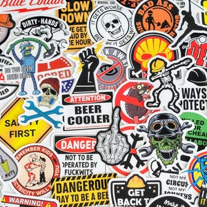 May include: A collection of assorted vinyl stickers featuring various graphic designs, including warning signs, cartoon characters, skulls, skeletons, tools, and humorous text phrases in a mix of black, white, yellow, red, and blue colors.