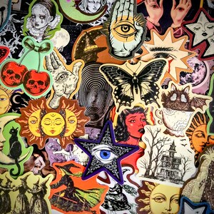 May include: A collection of assorted stickers featuring various illustrations including a black butterfly, a blue eye inside a purple star, skull cherries, a sun face, a black cat on a crescent moon, a haunted house, and a bat in a teacup.