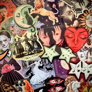 May include: A collection of assorted stickers featuring mystical and celestial imagery, including a red heart face, a lion, crescent moons, suns, stars with faces, butterflies, black cats, and figures in dark, illustrative, and surreal artistic styles.