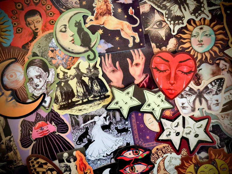 May include: A collection of assorted stickers featuring mystical and celestial imagery, including a red heart face, a lion, crescent moons, suns, stars with faces, butterflies, black cats, and figures in dark, illustrative, and surreal artistic styles.