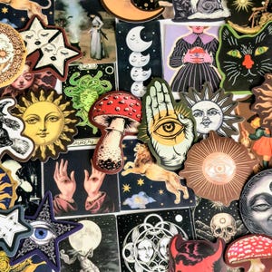 May include: A collection of assorted stickers featuring mystical and celestial imagery, including suns, moons, stars, mushrooms, eyes, hands, a lion, and a skull. The stickers display various artistic illustrations in a mix of colors and black and white.