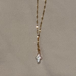 May include: Gold-colored necklace with a delicate chain and a cross pendant. The cross is a light, pearly color, and the chain has a repeating oval and rectangular link design. The necklace is displayed against a neutral background.