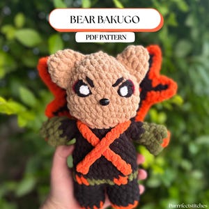 May include: A crocheted bear plushie in a black and orange outfit, with a stern expression. The bear has tan fur, white eyes, and a black nose. The text "BEAR BAKUGO" and "PDF PATTERN" are displayed on the image.
