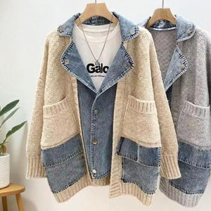 以下が含まれることがあります： 木製のハンガーに掛けられた2つの女性用ジャケット。1つはベージュでデニムのアクセントとポケットがあり、もう1つはグレーです。ベージュのジャケットはデニムの襟と前面にデニムパネルが付いています。「Galo」という文字が入った白いTシャツが見えます。