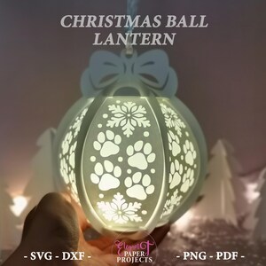 May include: A white Christmas ball lantern with paw prints and snowflake cutouts. The lantern has a bow at the top and the text "CHRISTMAS BALL LANTERN". The lantern is lit from within, creating a soft glow.