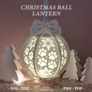 May include: A white Christmas ball lantern with paw prints and snowflake cutouts. The lantern has a bow at the top and is suspended by a silver ribbon. The text "CHRISTMAS BALL LANTERN" is at the top. The lantern is surrounded by white paper Christmas trees.