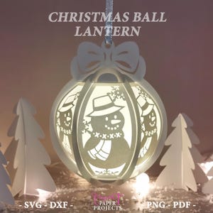 May include: A white Christmas ball lantern with a snowman design, the text "CHRISTMAS BALL LANTERN" is at the top. The lantern has a bow at the top and is hanging from a silver ribbon. The lantern is surrounded by white paper trees.