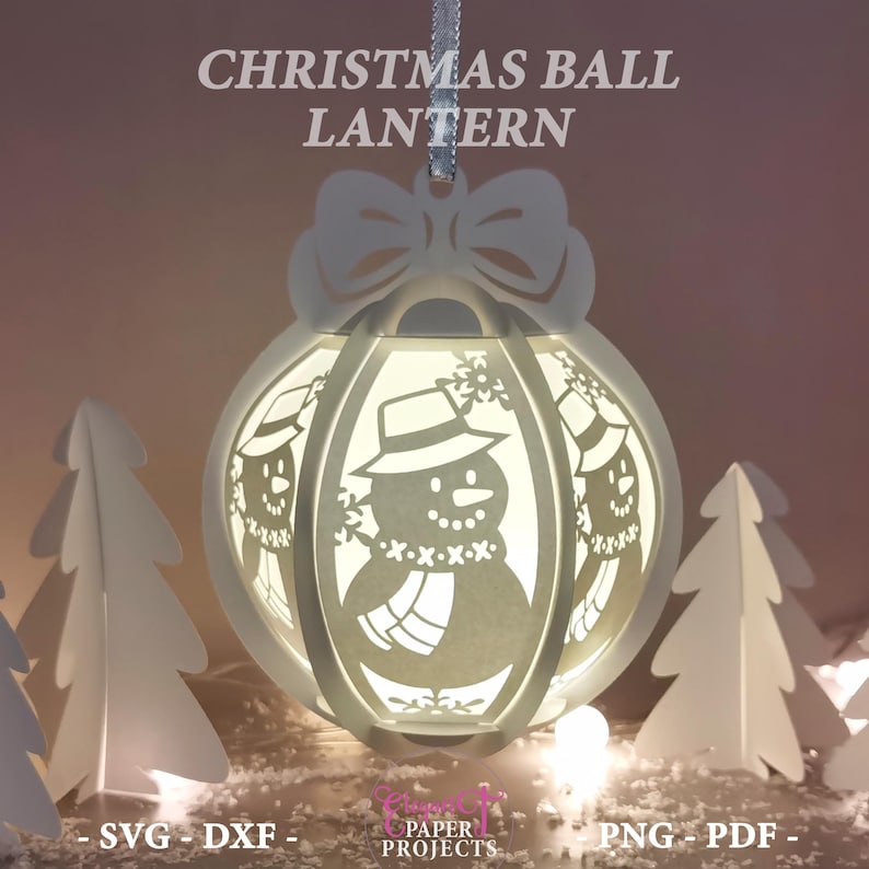 May include: A white Christmas ball lantern with a snowman design, the text "CHRISTMAS BALL LANTERN" is at the top. The lantern has a bow at the top and is hanging from a silver ribbon. The lantern is surrounded by white paper trees.