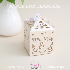 Op de afbeelding: Een crèmekleurige gunstdoos met ingewikkelde uitgesneden ontwerpen en de woorden "Mr & Mrs" op de voorkant. De doos is vastgebonden met een wit lint. Tekst bovenaan luidt "FAVOR BOX TEMPLATE". De onderkant van de afbeelding heeft tekst die luidt "SVG - DXF -" en "- PNG - PDF -".