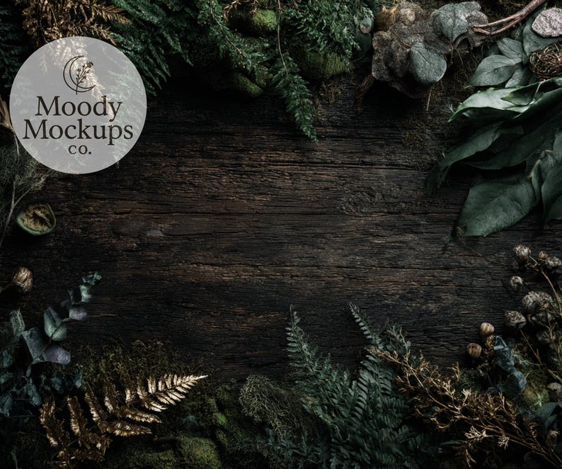 May include: Dark, textured wooden surface with a border of green foliage, moss, and dried plants. The image features the text "Moody Mockups co." in a circular logo, creating a natural, rustic aesthetic, suitable for product displays.