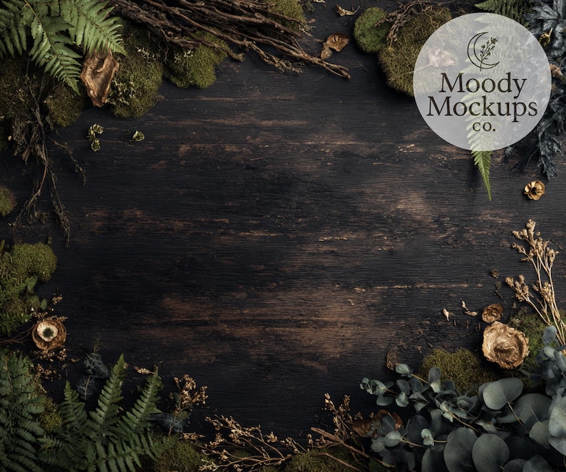 May include: Dark wood background with a natural, rustic aesthetic. The image features a variety of green ferns, moss, and dried plants arranged around the edges. A circular logo with the text "Moody Mockups co." is visible.