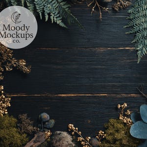 May include: Dark wood background with a circular logo that says "Moody Mockups co." The background is framed with green ferns, gold-colored branches, moss, and blue-green leaves.