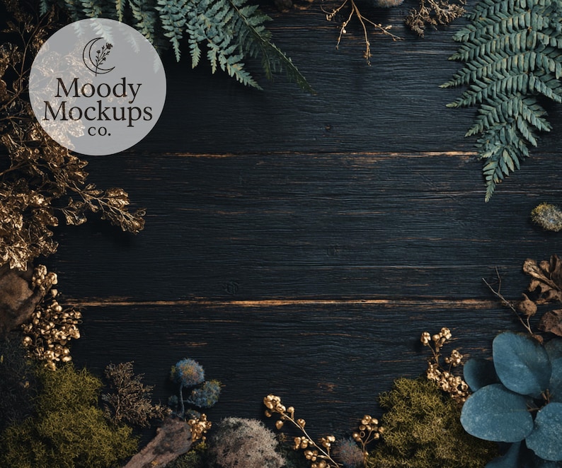 May include: Dark wood background with a circular logo that says "Moody Mockups co." The background is framed with green ferns, gold-colored branches, moss, and blue-green leaves.