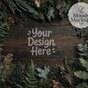 May include: A rustic wooden surface surrounded by green foliage, ferns, and moss. The text "Your Design Here" is displayed in a light font. A circular logo with the text "Moody Mockups Co." is in the upper right corner.