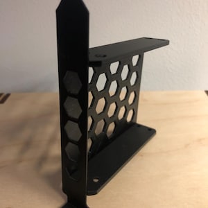 Op de afbeelding: Een zwarte, 3D-geprinte beugel met een honingraatpatroon en een montage-lip. De beugel heeft een rechthoekige basis en een verticale steun met zeshoekige uitsparingen. Het ontwerp is strak en modern.