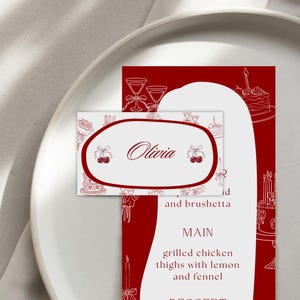 May include: A red and white place setting with a menu and name card. The menu features a list of dishes, including grilled chicken thighs. The name card says "Olivia" in cursive.