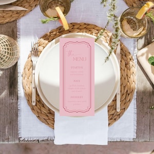 Może przedstawiać: Różowa karta menu z napisem "The Menu" leży na białym talerzu, będąc częścią nakrycia stołu. Menu zawiera opcje przystawek, dań głównych i deserów. Nakrycie obejmuje tkane podkładki, sztućce i szklanki z napojami.