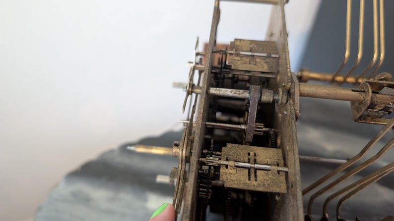 May include: Close-up of a vintage clock mechanism, showcasing intricate gears, levers, and springs. The aged brass components are visible, with a focus on the mechanical details. The clock's internal structure is partially exposed, revealing its complex design.