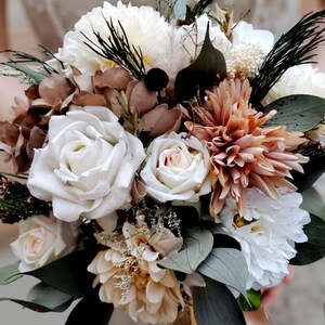 May include: A wedding bouquet with white roses, peach dahlias, and assorted flowers and foliage. The arrangement includes brown and cream-coloured blooms, dark green leaves and stems. The bouquet is tied with a ribbon.