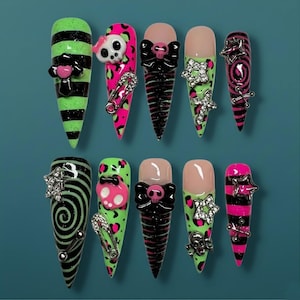 Könnte beinhalten: Ein Set aus zehn langen, spitz zulaufenden Kunstnägeln im Punkrock-Stil. Designs umfassen neongrüne und schwarze Streifen, pinkfarbenen Leopardenmuster, Totenköpfe, Schleifen und silberne Verzierungen. Einige Nägel weisen Sicherheitsnadeln und Sternakzente auf.