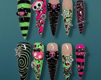May include: A set of ten long, pointed false nails with a punk rock theme. Designs include neon green and black stripes, pink leopard print, skulls, bows, and silver embellishments. Some nails feature safety pins and star accents.