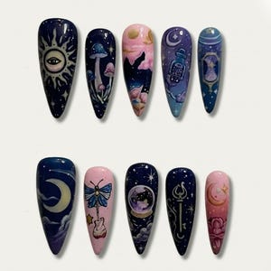 May include: A set of ten long, pointed artificial nails with celestial and fantasy-themed designs. The nails feature images of moons, stars, mushrooms, butterflies, and a snow globe, in shades of blue, pink, and purple.