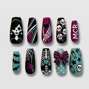 May include: A set of ten press-on nails featuring various designs including a skull character, diagonal stripes, a skeleton hand holding a heart, skulls with bows, the text MCR, bats, a spider web, a skeleton ribcage, a 3D bow, and safety pins.