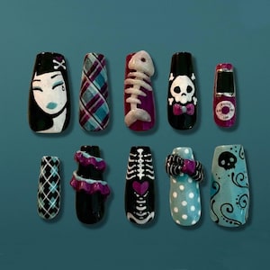 May include: A collection of ten press-on nails with various designs. The designs include a crying woman, plaid, a fish skeleton, a skull with a bow tie, a retro phone, a diamond pattern, ruffles, a rib cage, polka dots, and a skull with swirls.