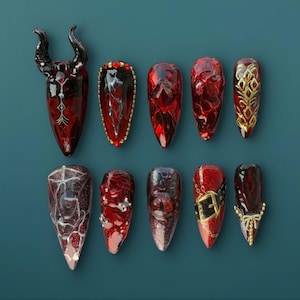 May include: A collection of ten long, pointed, artificial nails in various designs. The nails are primarily red, with accents of gold, black, and silver. Some nails feature intricate patterns, while others have decorative elements like horns and buckles.