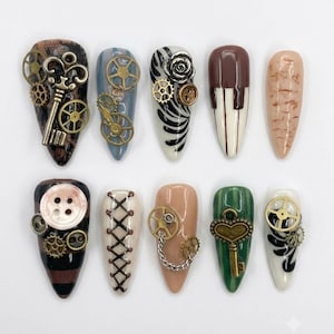 Puede incluir: Un conjunto de diez uñas postizas en forma de almendra con diversos diseños que incluyen engranajes metálicos, llaves antiguas, botones, cordones tipo corsé y patrones complejos en tonos marrón, negro, crema, verde y nude con acabado brillante.