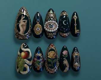 Puede incluir: Uñas de color verde oscuro con marcos dorados ornamentados y varios diseños. Los diseños incluyen una mano sosteniendo un anillo, un ojo, una luna creciente, una llave, una serpiente con fruta, una rosa y un reloj de arena. Las uñas son almendradas.