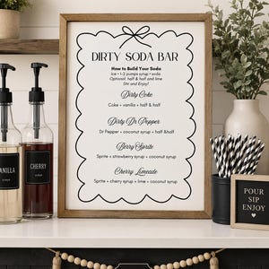 Puede incluir: Un letrero enmarcado titulado DIRTY SODA BAR con instrucciones y recetas para Dirty Coke, Dirty Dr Pepper, Berry Sprite y Cherry Limeade. El letrero presenta un borde festoneado y un gráfico de lazo, exhibido junto a botellas de jarabe.