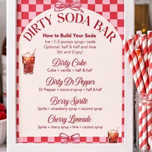 May include: A framed sign with a red and white checkered background and the words "Dirty Soda Bar" in a decorative font. The sign lists soda recipes like Dirty Coke and Berry Sprite. Red and white striped straws are in a glass jar.