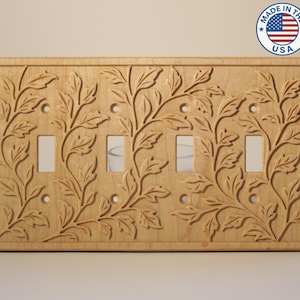 May include: A light-colored wooden wall plate for four toggle switches, featuring an intricate carved leaf and vine pattern across the entire surface. The rectangular cover includes eight screw holes and four rectangular cutouts.