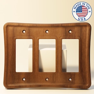 May include: A wooden triple switch plate with a curved design. The plate is a warm brown color and has three rectangular openings for the switches. The words "MADE IN THE USA" are printed on a circular sticker with the American flag.