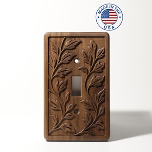 Peut inclure: Un cache-interrupteur rectangulaire en bois avec un motif de feuilles et de vignes sculptées. Le couvercle comporte une ouverture pour un seul interrupteur et deux trous de vis. L'inscription "MADE IN THE USA" est imprimée sur un autocollant circulaire.