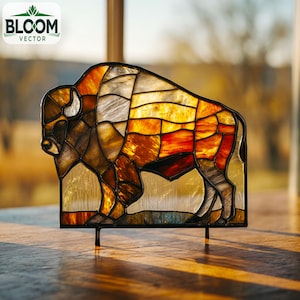 May include: Stained glass bison sculpture with a black metal frame. The bison is composed of various shades of brown, orange, and yellow glass, creating a warm, inviting glow. The Bloom Vector logo is in the upper left corner.