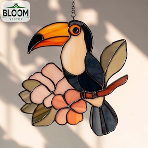 Könnte beinhalten: Buntglas-Tukan mit orangefarbenem Schnabel, der auf einem Ast mit Blumen sitzt. Der Vogel hat einen schwarzen Kopf und einen dunkelblauen Körper. Die Blumen sind rosa und orange. Das Bloom Vector-Logo befindet sich oben links.