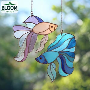 Puede incluir: Dos adornos de peces de vidriera, uno melocotón y lavanda, el otro azul y verde azulado, cuelgan de cadenas. Los peces tienen aletas y colas detalladas, con un contorno color cobre. El logotipo de Bloom Vector está en la esquina superior izquierda.