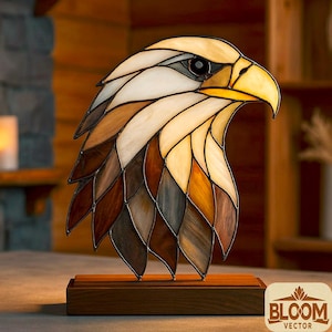 May include: Stained glass eagle head sculpture with a wooden base. The eagle's head features a variety of colors, including white, brown, and yellow. The sculpture is designed with a detailed, artistic style, and is a decorative item.
