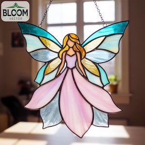 Pode incluir: Apanhador de sol de fada de vitral com um vestido rosa e asas azuis e amarelas. A fada tem cabelo loiro e está pendurada por uma corrente. O logotipo Bloom Vector está no canto superior esquerdo.