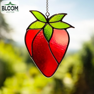 May include: A stained glass strawberry suncatcher with a red body and green leaves. The suncatcher is hanging from a chain. The logo "BLOOM VECTOR" is in the upper left corner.