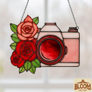 May include: A stained glass camera design with red roses and green leaves. The camera is pink with a red lens and is suspended by a chain. The design includes the text "BLOOM VECTOR" in a brown logo.