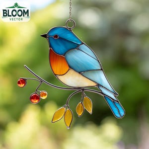 May include: Stained glass bird decoration in shades of blue, orange, and white, perched on a metal branch with red berries and yellow leaves. The bird is suspended by a chain. The Bloom Vector logo is in the upper left corner.
