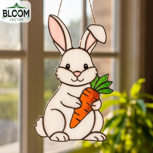 Peut inclure: Un lapin de Pâques en vitrail tenant une carotte. Le lapin est blanc avec l'intérieur des oreilles rose et un nez rose. La carotte est orange avec des feuilles vertes. Le texte "BLOOM VECTOR" est visible.